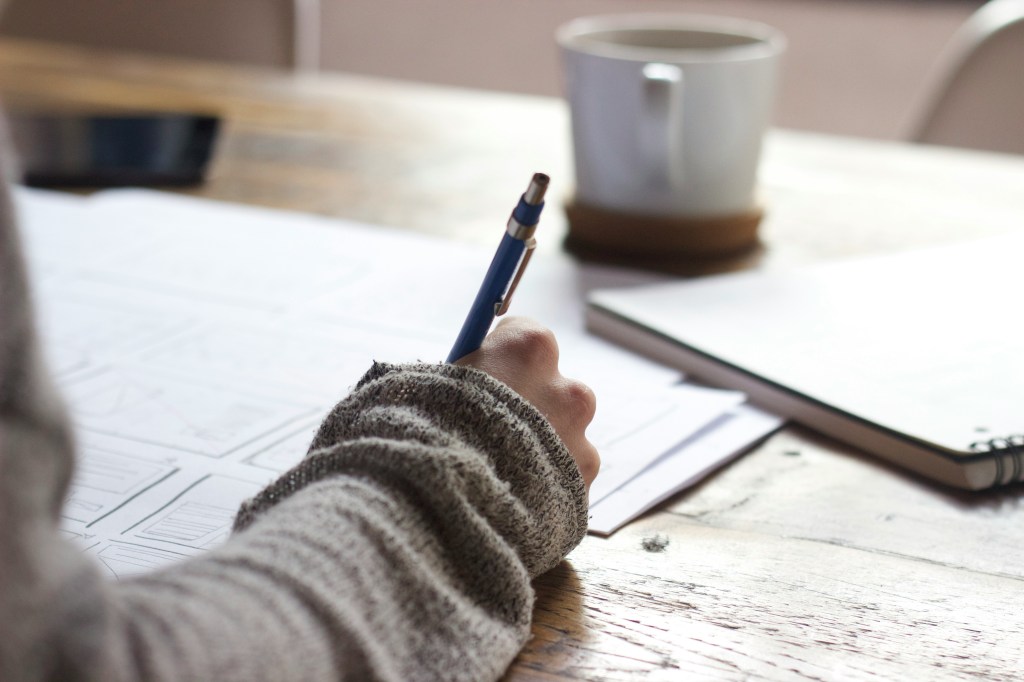 Woman writing with pen on paper in free grant writing classes. 